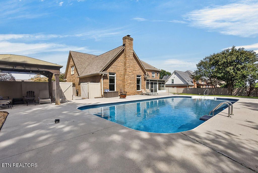 Saltwater in-ground pool and pool deck behind the all-brick home at 12736 Broken Saddle Rd, with a pergola and privacy fence, in Fort West, Knoxville, TN
