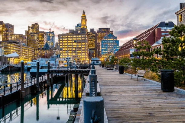 Wooden boardwalk along Boston’s waterfront with downtown buildings at dusk
