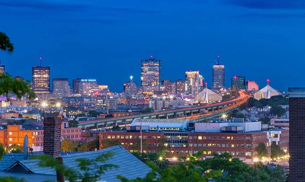 Boston skyline at dusk, with a bridge and illuminated buildings