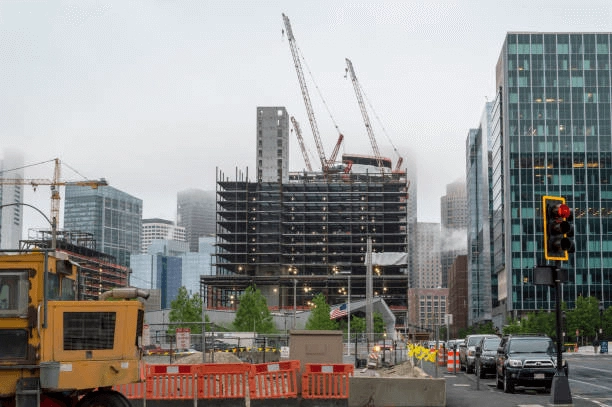 Tower cranes above an unfinished multistory building beside a city street.