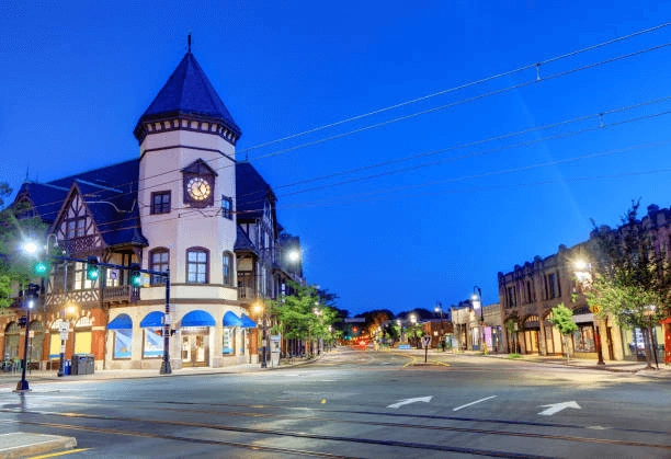 Clock-tower corner building and storefronts at a street intersection at dusk.