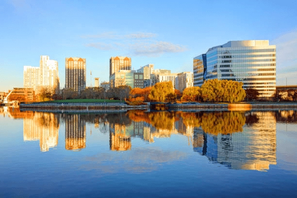 Waterfront buildings and autumn trees reflected in calm water.
