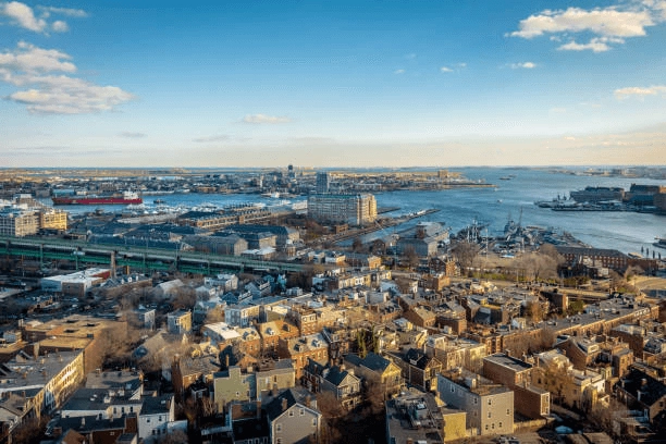 Elevated view of brick neighborhood blocks, roads and a harbor with ships.