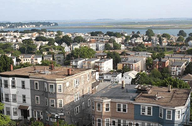 Residential rooftops and trees overlooking water and an airfield.