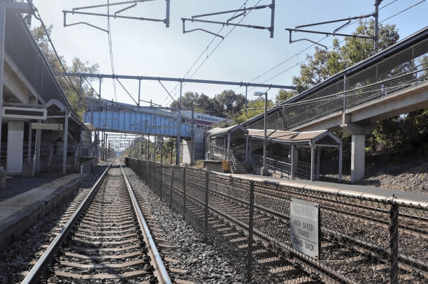 Rail tracks, station platforms and overhead wires beneath a pedestrian bridge.
