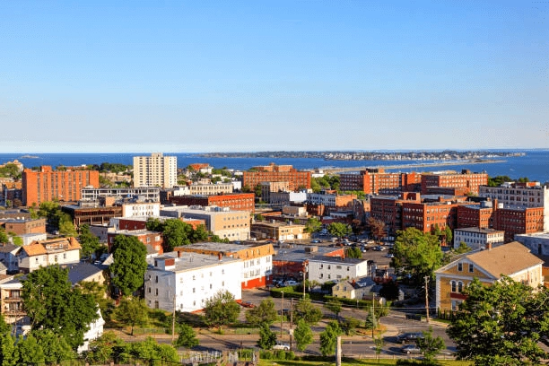 City buildings and residential rooftops with water in the distance.