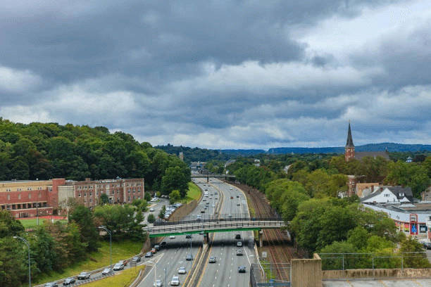 Highway and adjacent rail tracks running between buildings and trees.