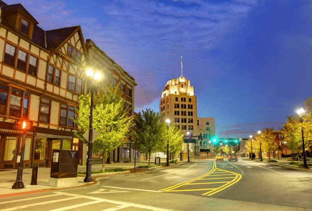 City street with trees, streetlamps and illuminated buildings at dusk.