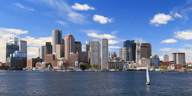 City skyline across harbor water with a sailboat