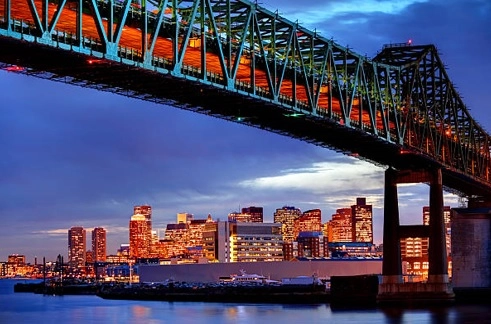 Steel truss bridge above water and an illuminated city skyline at dusk