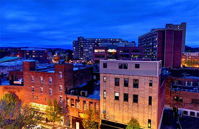 Brick rooftops and taller buildings under a blue evening sky