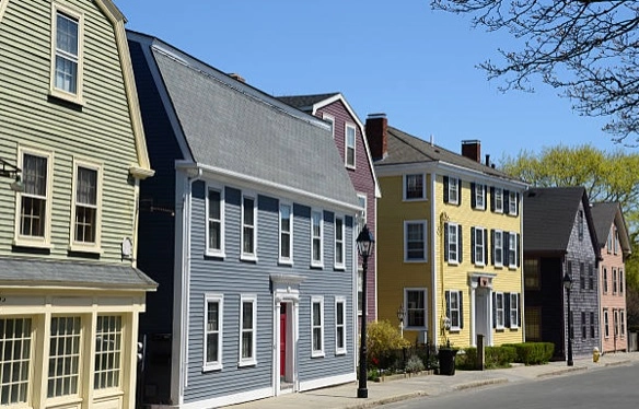 Pastel clapboard houses with shuttered windows beside a street and sidewalk