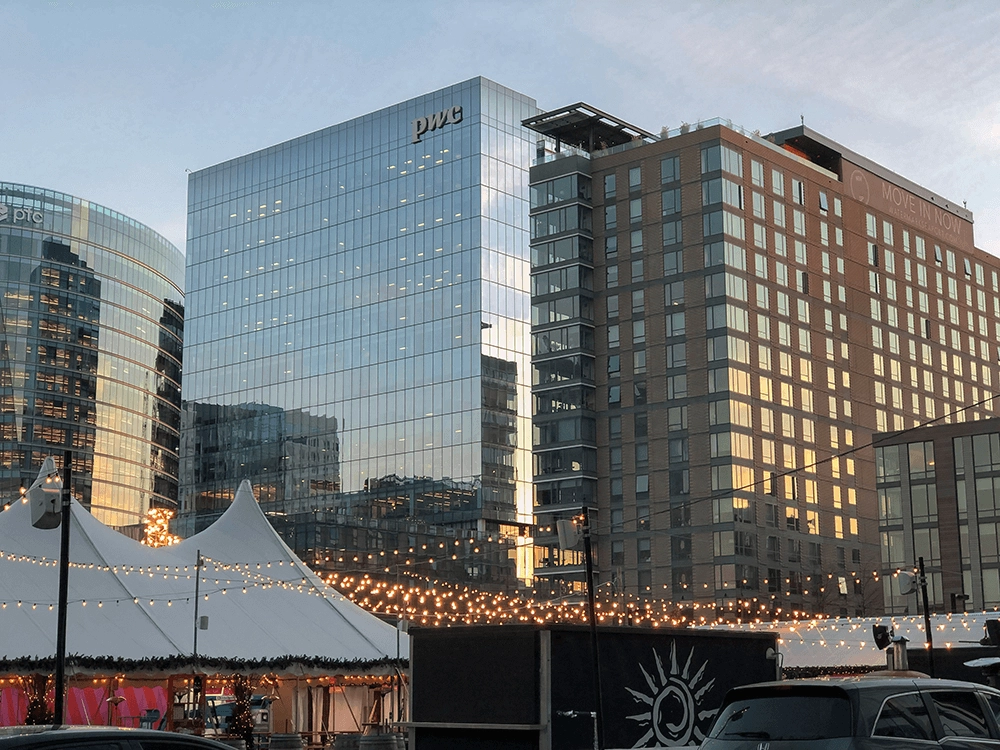 Glass and brick buildings behind white tents and strings of lights at dusk