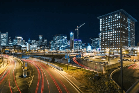 Nighttime streets with light trails, illuminated office buildings and a crane.