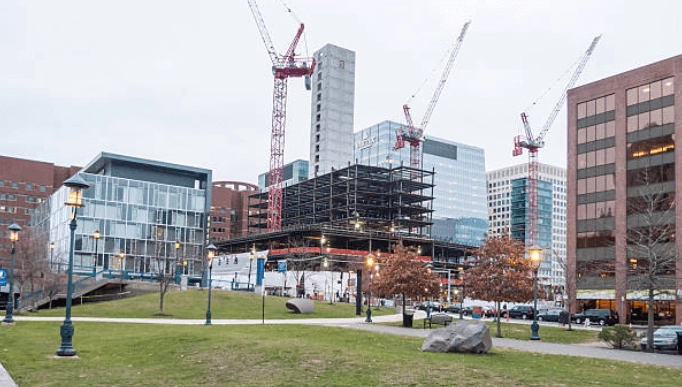 Construction cranes and an exposed building frame beside city buildings.