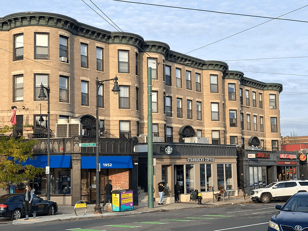 Bow-front buildings above storefronts, with vehicles and overhead wires.