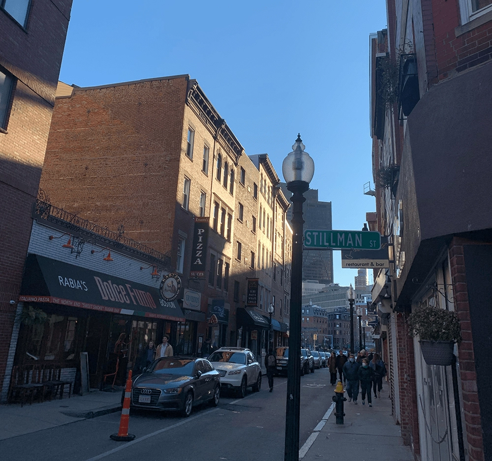 Brick-lined street with a Stillman Street sign, shops and pedestrians