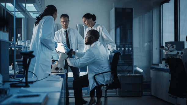 People in lab coats discussing work at a laboratory bench