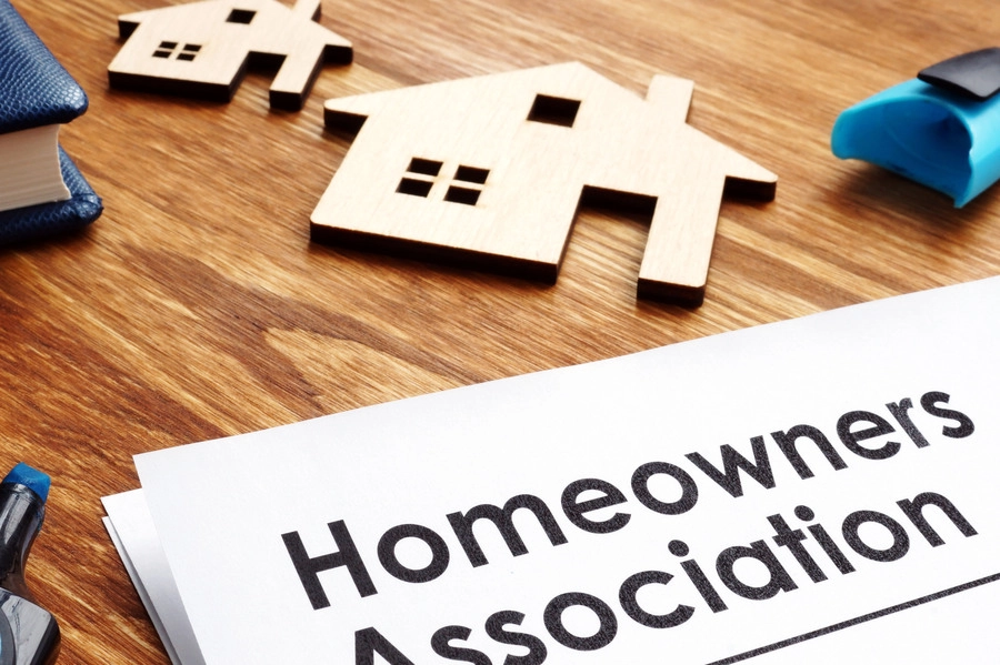 A piece of paper titled "Homeowners Association" sitting next to a blue highlighter, wooden home cutouts, and a book.