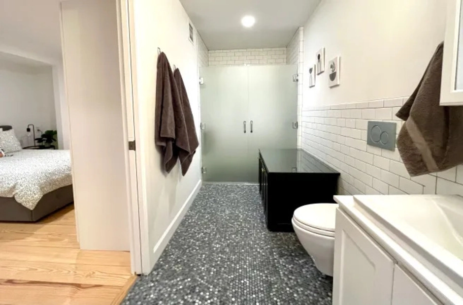 Unit One — Ground-Floor Comfort Curbless walk-in shower with teak seat and penny-tile floor in Unit One bathroom.