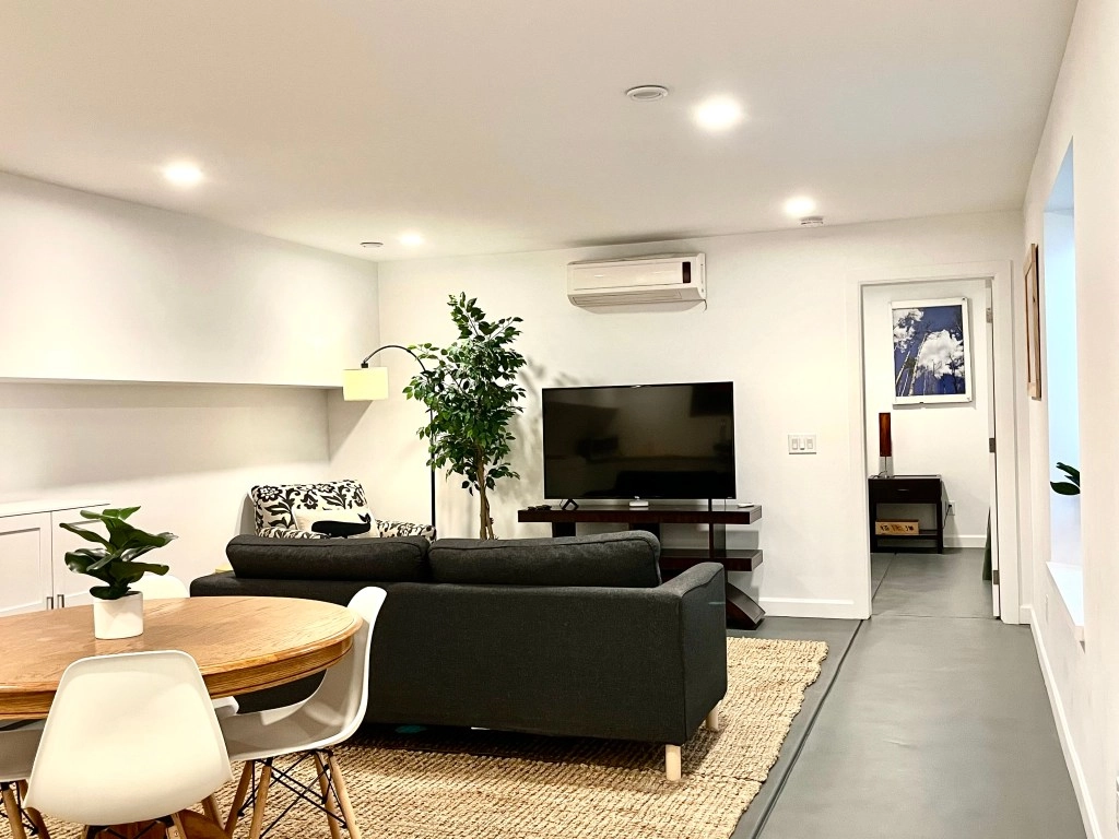Unit Three — The Garden-Level Retreat Garden-level living room with open layout, large window, and natural textures.