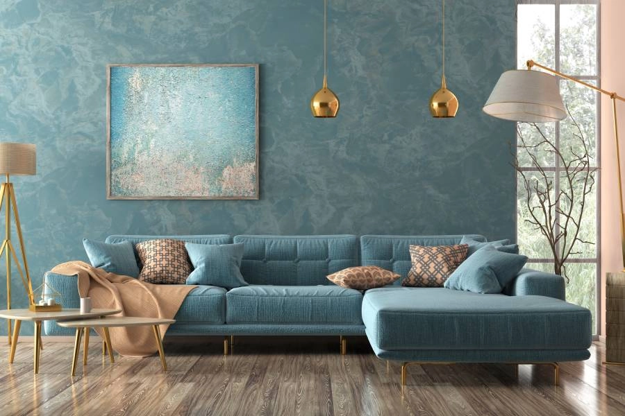 A living room with a textured blue accent wall, a blue L-shaped couch, two gold floor lamps, and two gold pendant lamps.