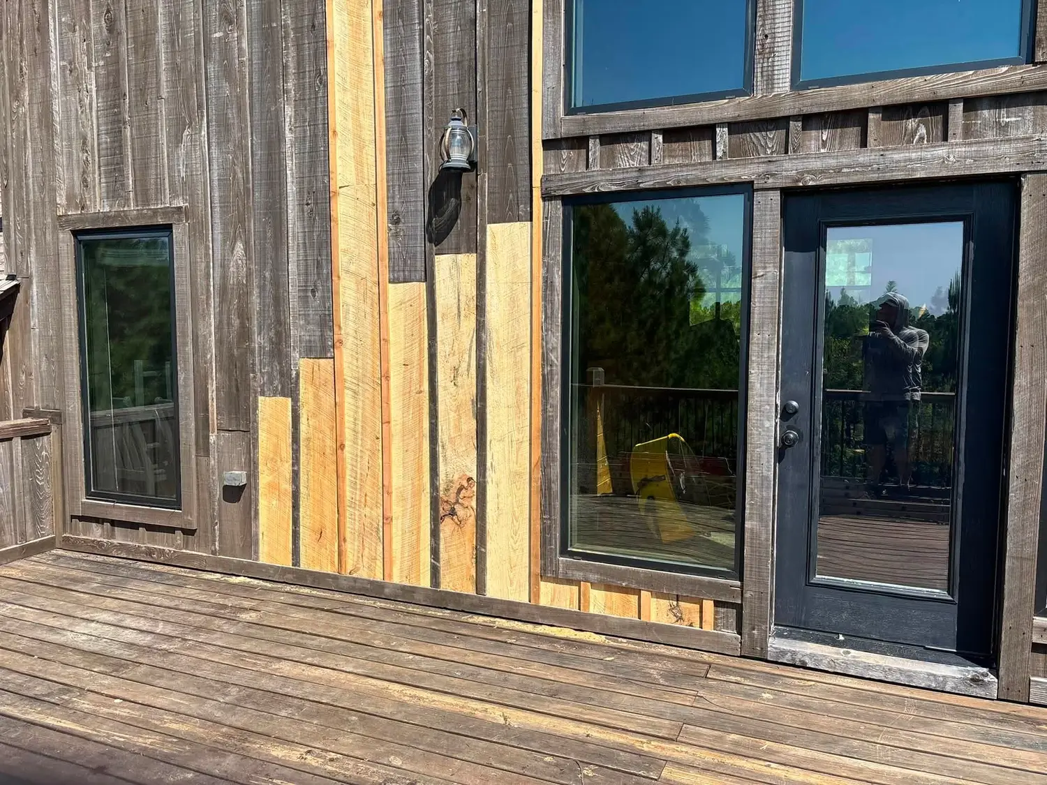 Replaced board and batten siding next to a cabin deck and glass door, exterior repair by Kiamichi Custom Homes and Remodeling