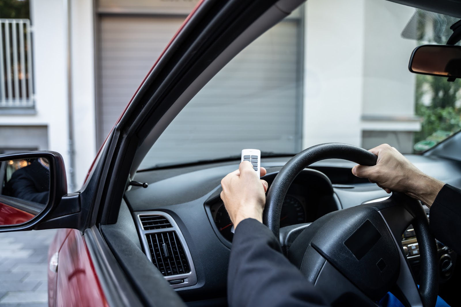 A person uses a wireless controller in their car to open their garage door.