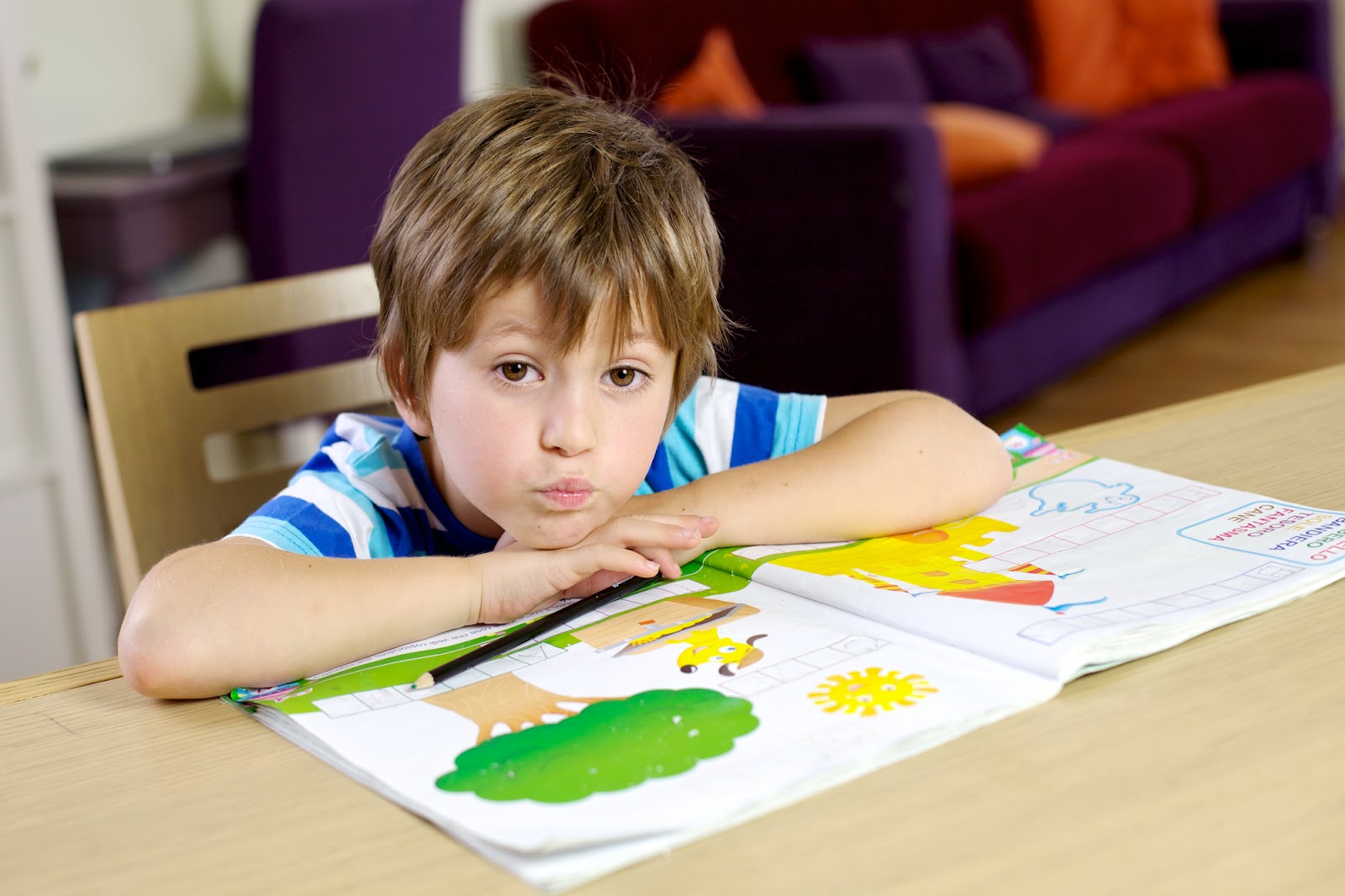 A happy child rests their head on their hands, on top of a coloring book.