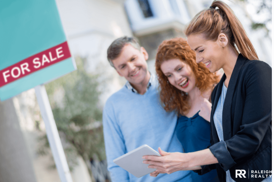 For sale sign in background as realtor answers buyer's questions 