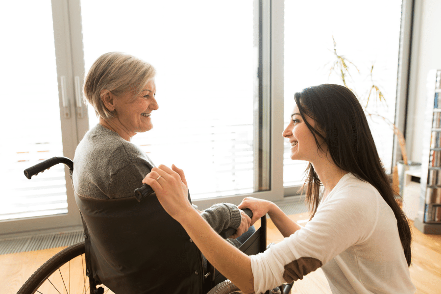 A happy elderly woman in a wheelchair with a girl kneeling next to her