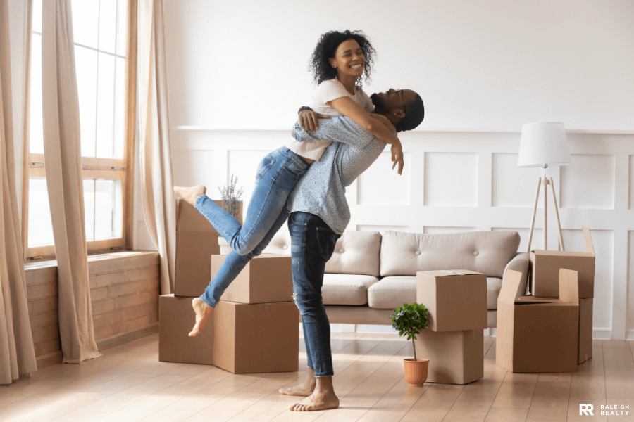 A happy couple who have just moved into their first home hugging one another with moving boxes in the background