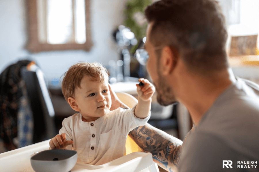 A little boy feeding his dad from his high-chair