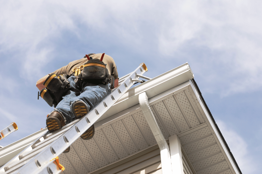 man standing on ladder and making repairs on the outside of a home