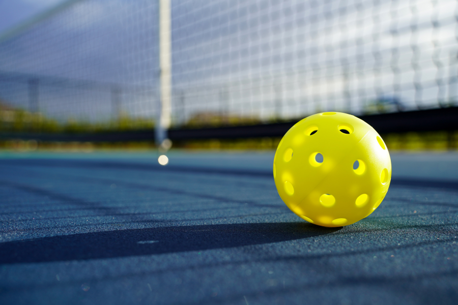 Yellow pickleball on blue court with net in back.
