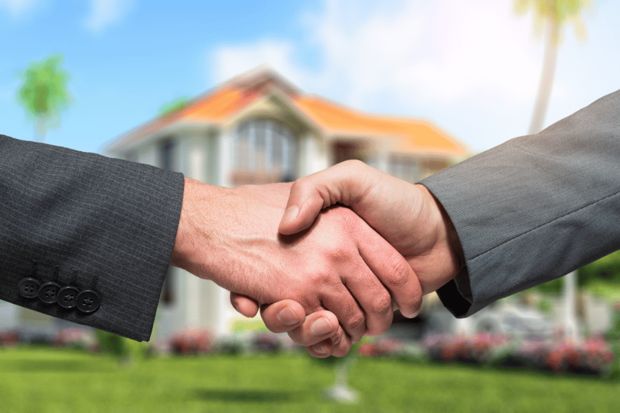 two mans shaking hands with a home in the background