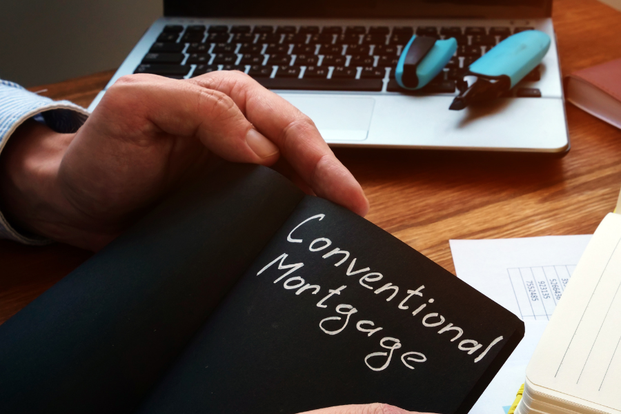 Blackboard with conventional mortgage written and hand with laptop and pens in the back