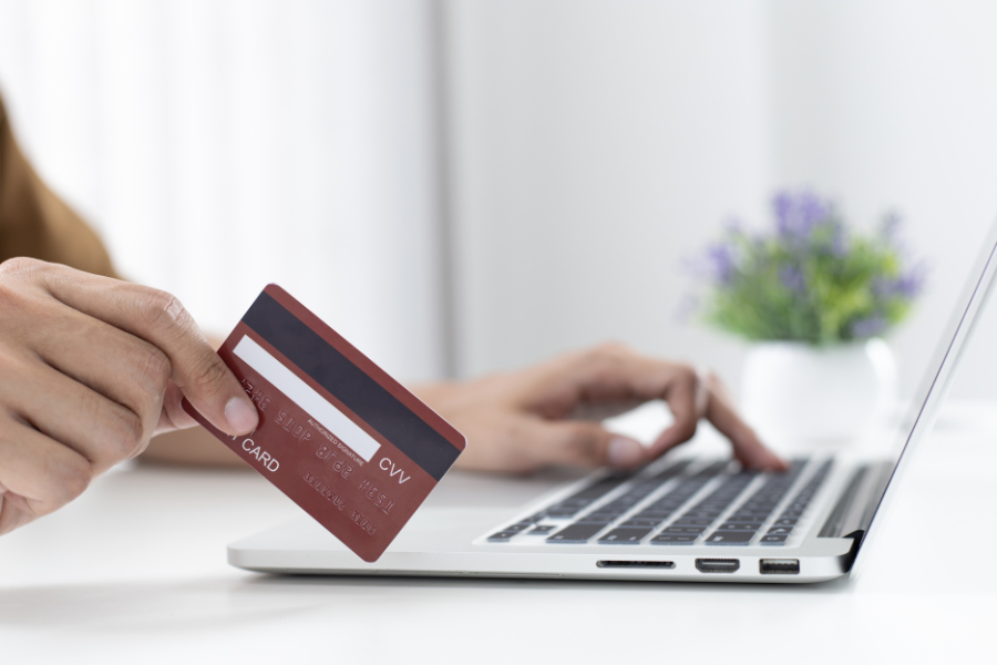 Hand holding red credit card with laptop and green plant