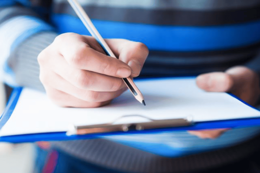 Writing with pencil on paper on a clipboard 