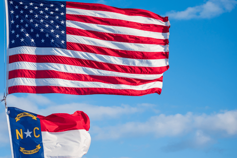 NC Flag and American Flag Blowing in the Wind on a Clear Day