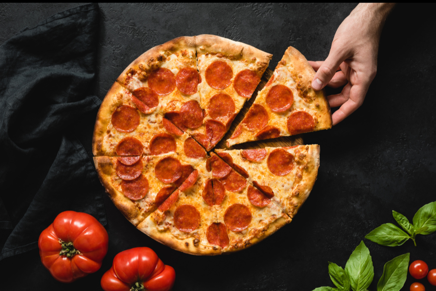 Pepperoni pizza on black surface with red bell pepper and fresh basil with cherry tomato