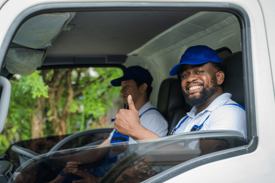 team of movers smiling and giving a thumbs up in the front of a moving truck