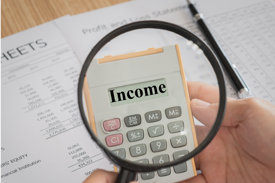 yellow and white calculator with income typed out and paperwork on table with black pen