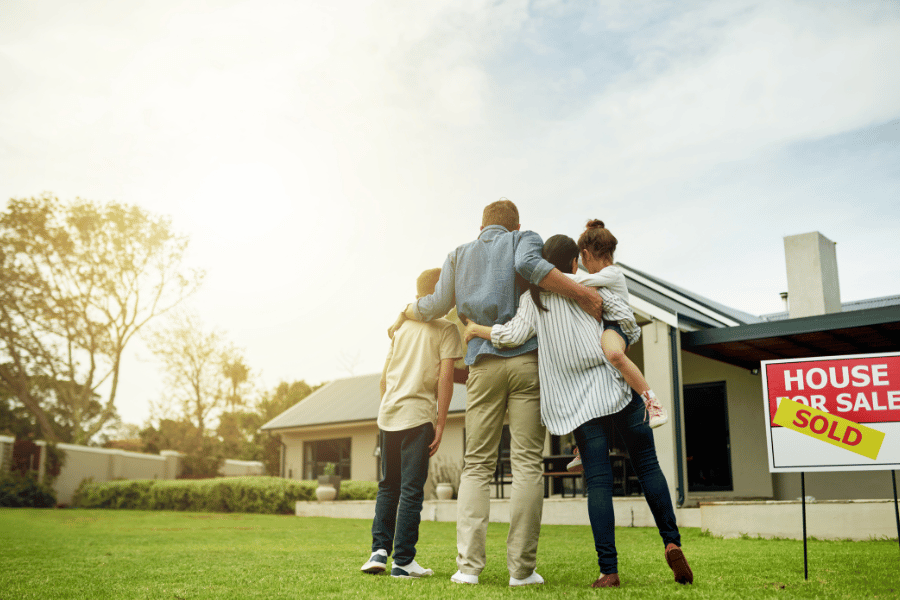 Family who bought their dream home with sold sign in foreground