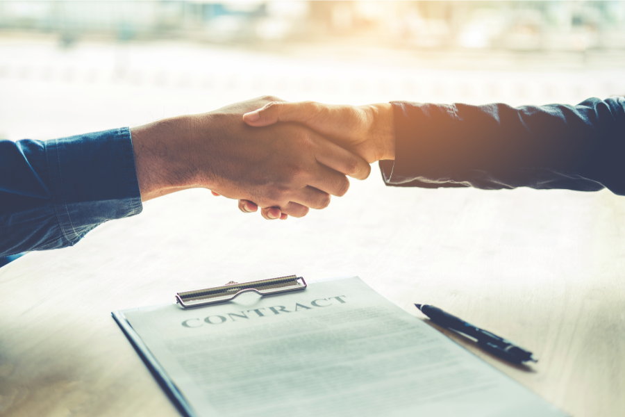 Two hands shaking with contract below