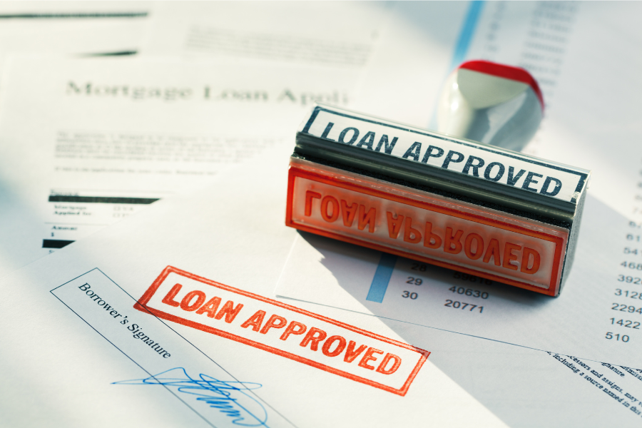 Stamper with loan approved written on it stamped in red ink on white paper with borrowers signature