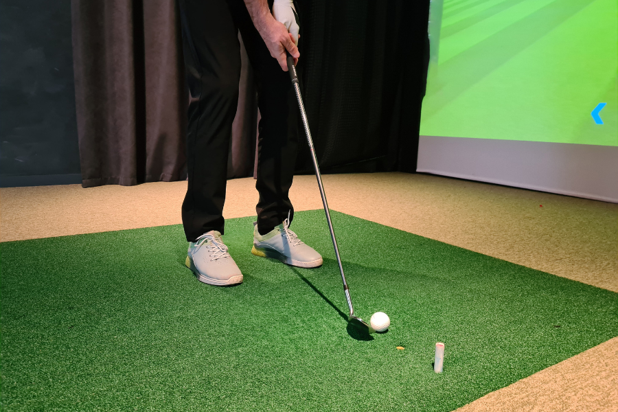 Mens shoes on green turf with golf club