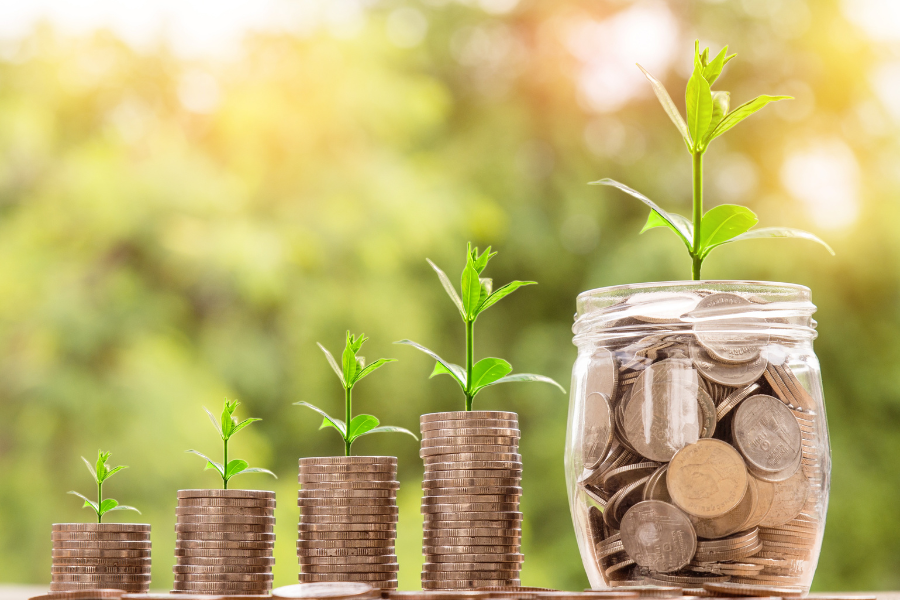 stacks of coins with green sprouting plants with jar of coins