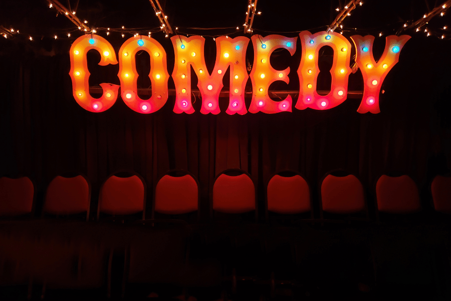 large light up comedy sign in front of stage with lots of seats 
