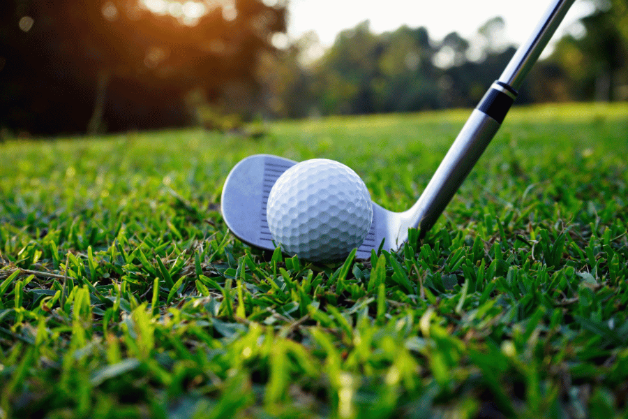 Golf ball and golf club on a green with the sunset 